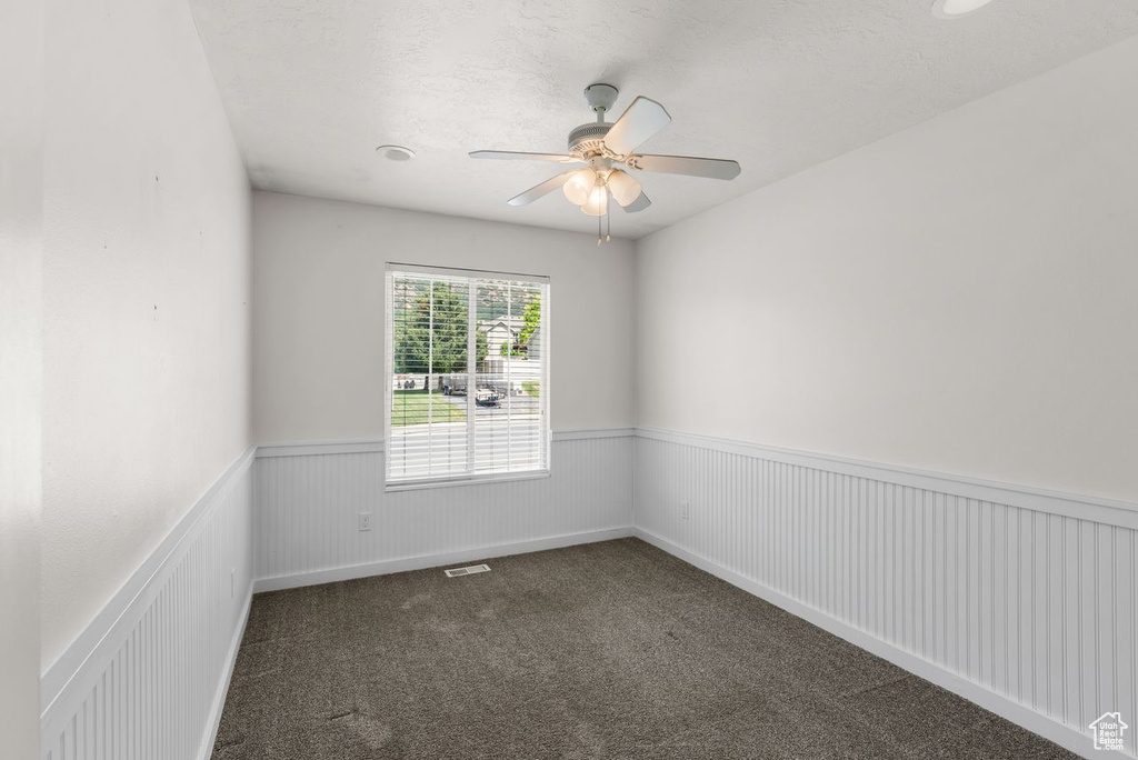 Spare room with a wainscoted wall, ceiling fan, and dark colored carpet