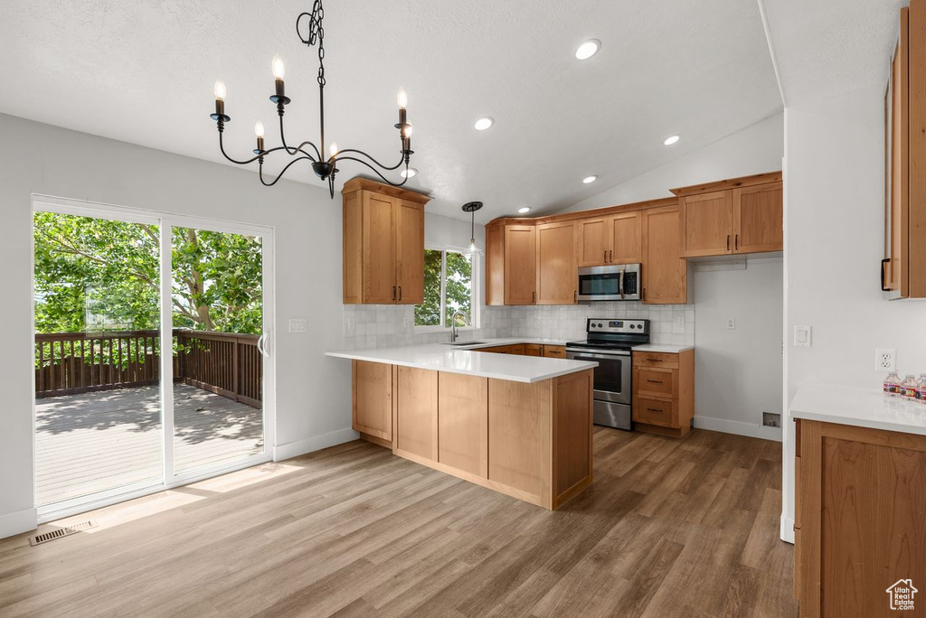 Kitchen featuring appliances with stainless steel finishes, a peninsula, decorative backsplash, brown cabinetry, and light wood-style floors