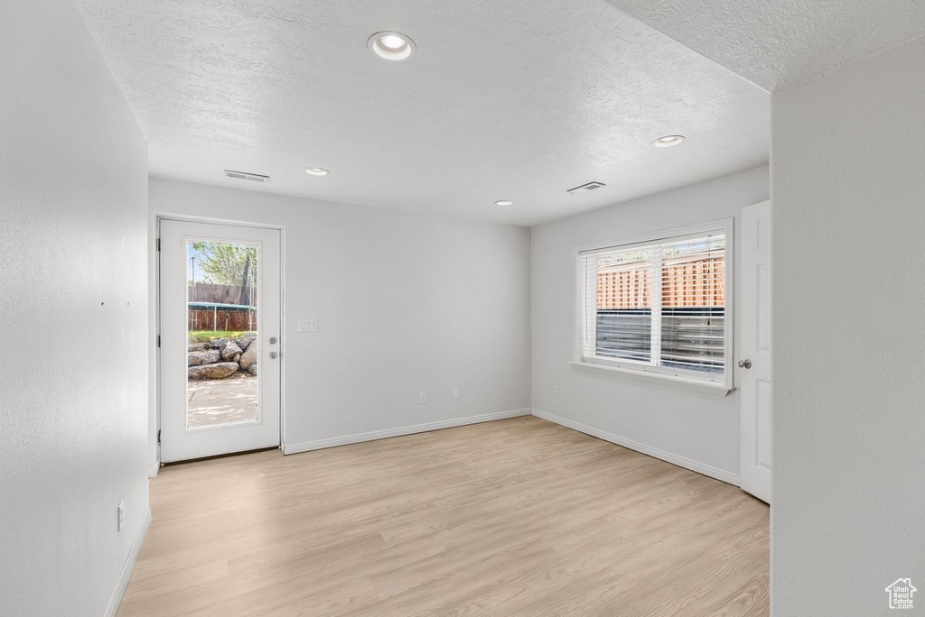 Empty room with a textured ceiling, light wood-style flooring, and recessed lighting