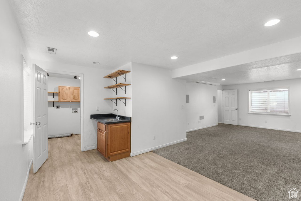 Unfurnished living room featuring bar with sink, recessed lighting, a textured ceiling, and light wood-style floors