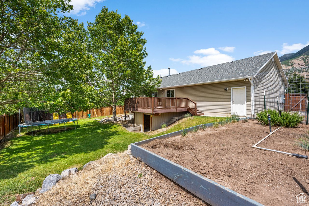 Fenced backyard with a deck, a trampoline, and stairs
