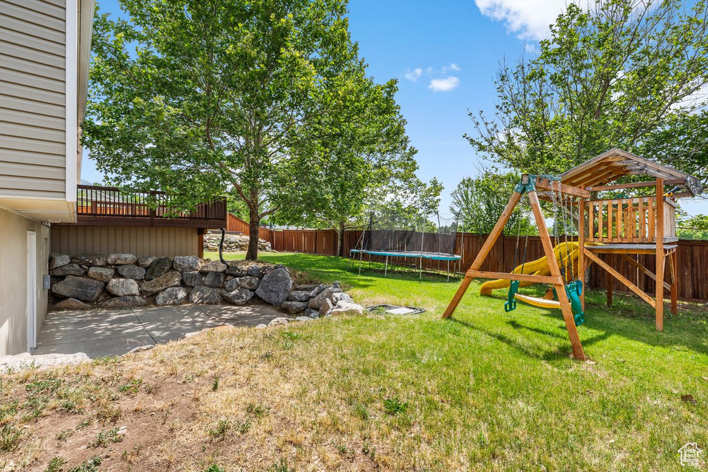 Fenced backyard featuring a trampoline and a playground