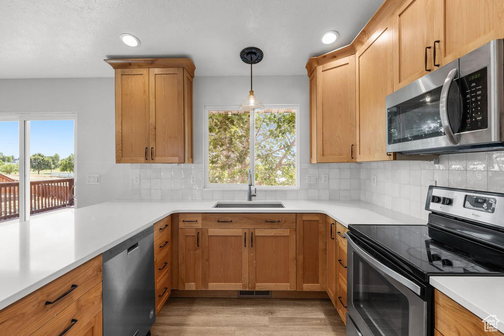 Kitchen featuring stainless steel appliances, light wood-style floors, light countertops, tasteful backsplash, and hanging light fixtures
