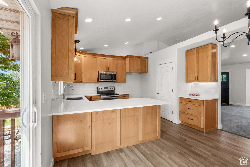 Kitchen with stainless steel appliances, a peninsula, backsplash, recessed lighting, and light countertops