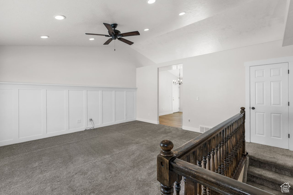Carpeted empty room with a ceiling fan, vaulted ceiling, recessed lighting, a chandelier, and a decorative wall