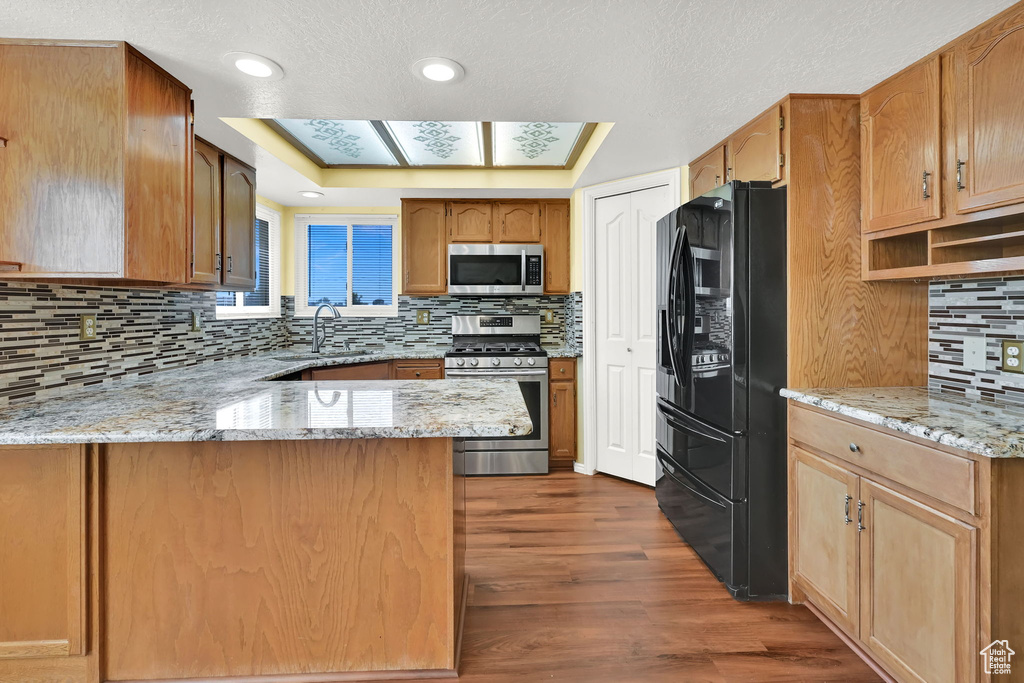 Kitchen featuring appliances with stainless steel finishes, backsplash, dark wood-type flooring, a peninsula, and light stone counters