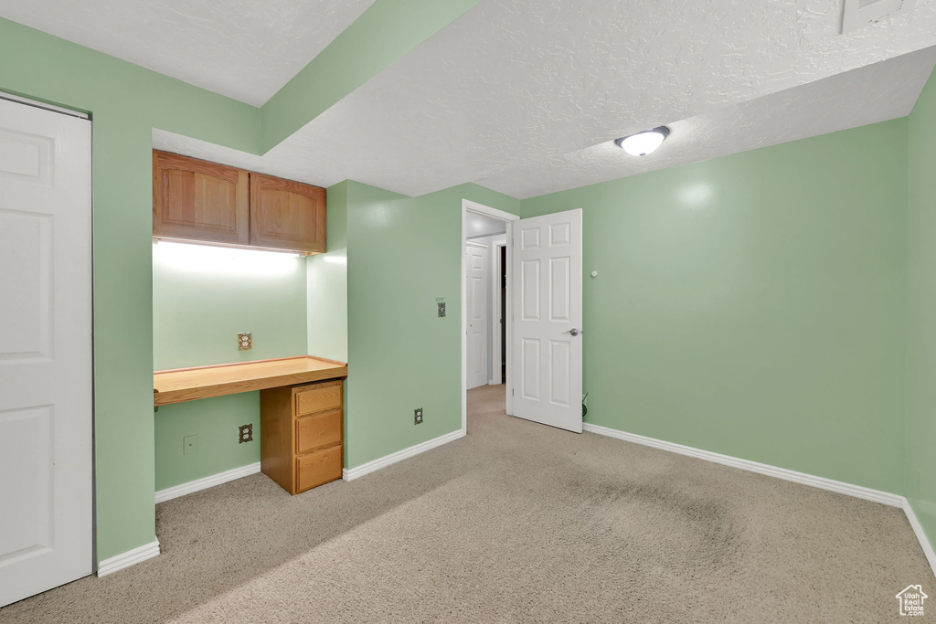 Unfurnished office with built in desk, light colored carpet, and a textured ceiling