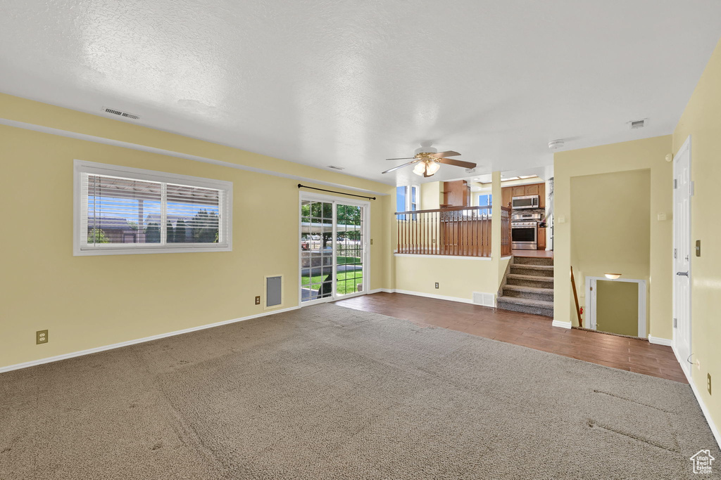 Unfurnished living room featuring carpet floors, stairs, and a ceiling fan