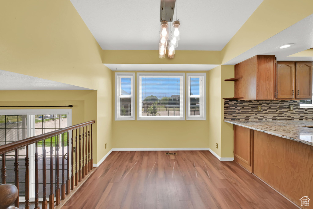Kitchen featuring wood finished floors, tasteful backsplash, brown cabinets, and light stone countertops