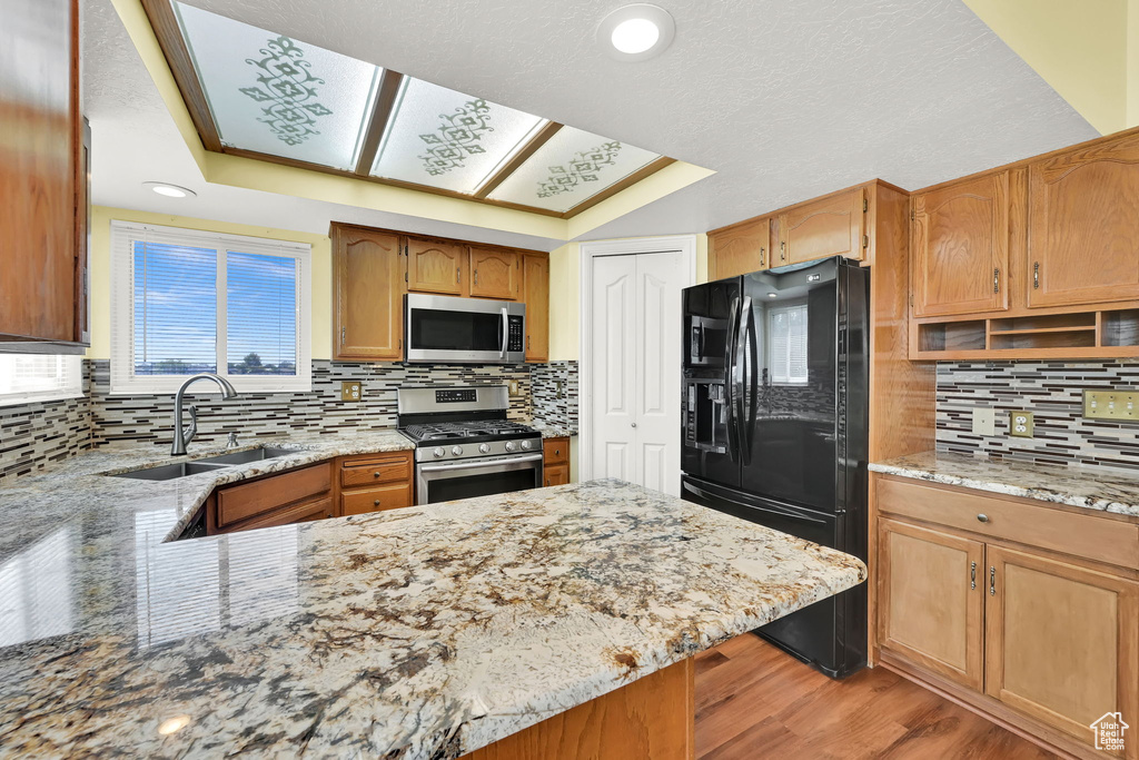Kitchen with appliances with stainless steel finishes, decorative backsplash, light stone counters, light wood-style flooring, and a peninsula