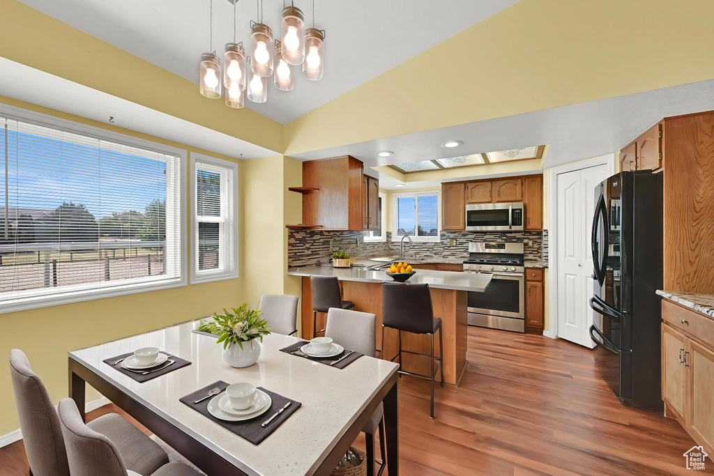 Kitchen featuring appliances with stainless steel finishes, a peninsula, decorative backsplash, a kitchen bar, and dark wood finished floors