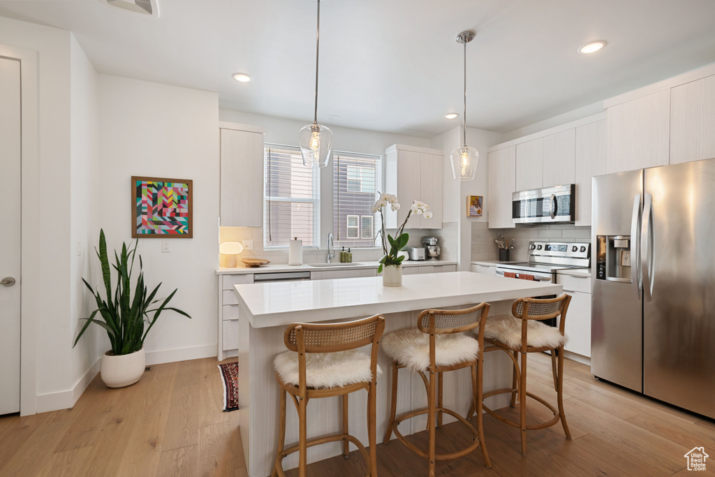 Kitchen featuring stainless steel appliances, a kitchen breakfast bar, tasteful backsplash, light countertops, and recessed lighting