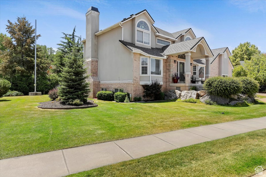 View of front of home with a chimney, a front yard, brick siding, and stucco siding