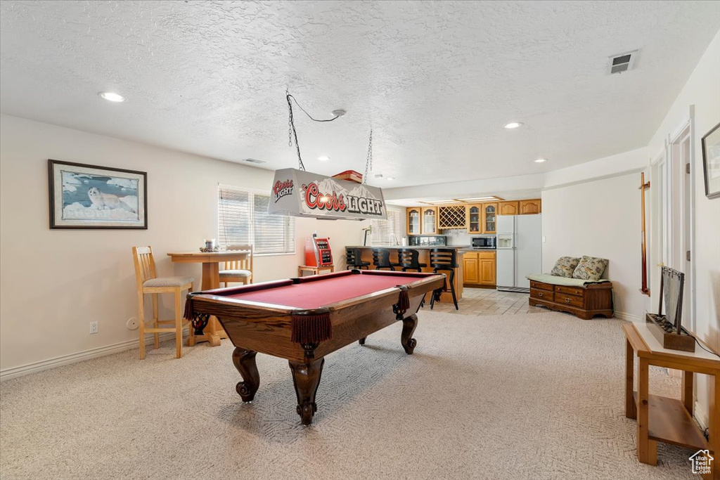 Game room featuring light carpet, bar with sink, a textured ceiling, pool table, and recessed lighting