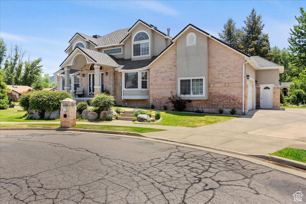 View of front of house featuring concrete driveway, brick siding, a garage, stucco siding, and a front lawn