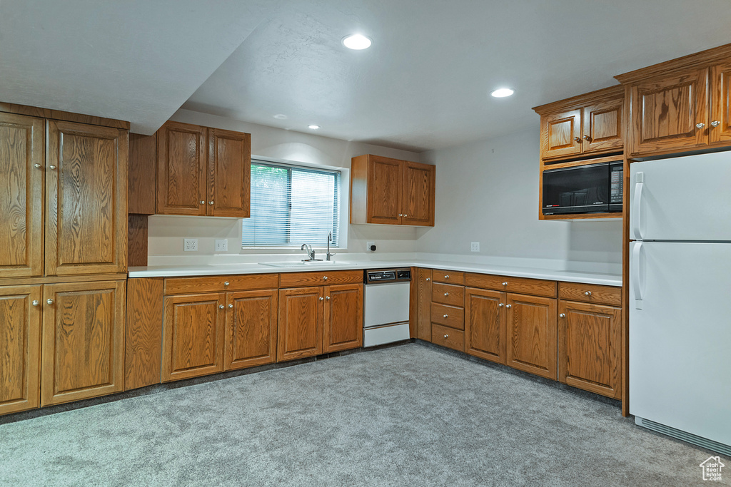 Kitchen featuring white appliances, brown cabinets, light colored carpet, recessed lighting, and light countertops