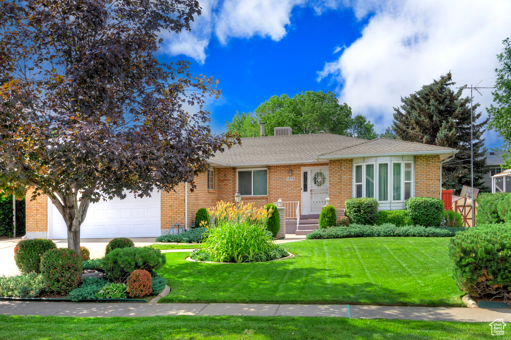 Ranch-style home with an attached garage, a front lawn, brick siding, and roof with shingles