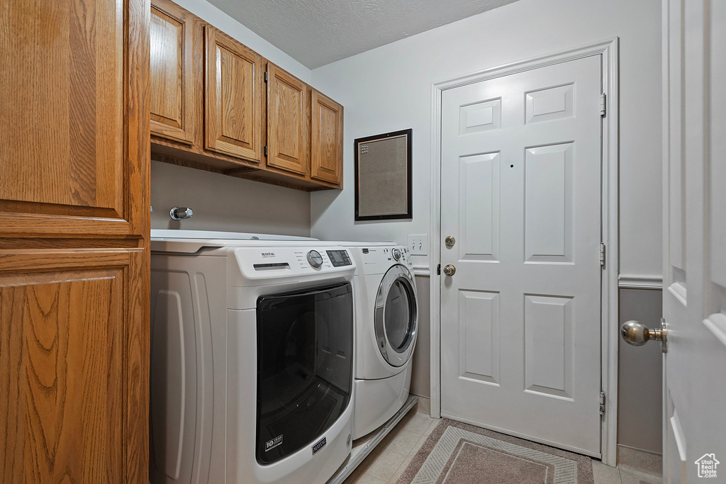 Laundry area featuring washing machine and dryer, cabinet space, and light tile patterned floors