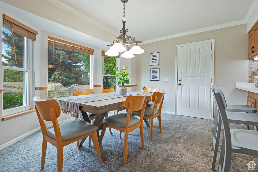 Carpeted dining area featuring a chandelier, ornamental molding, and healthy amount of natural light