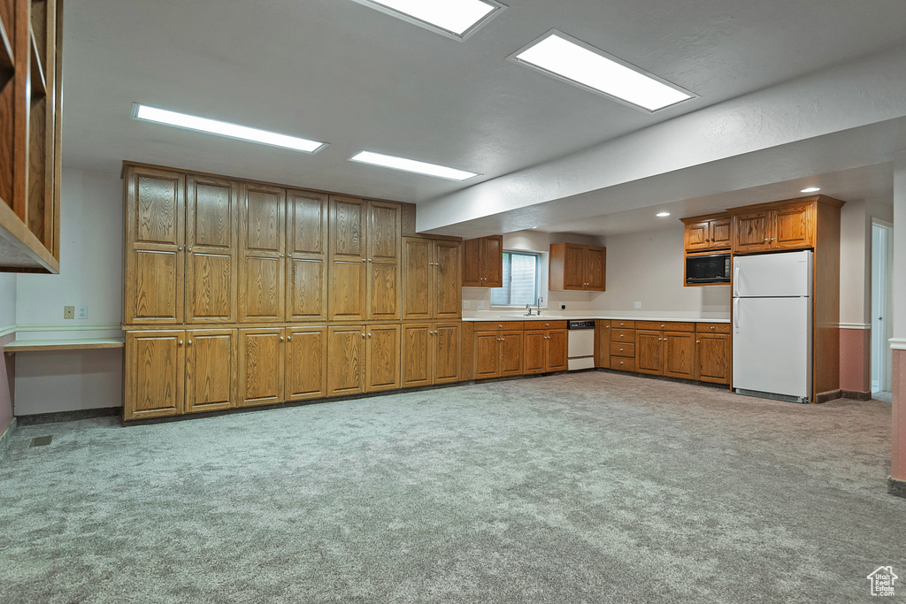 Kitchen with white appliances, brown cabinetry, light countertops, light carpet, and recessed lighting