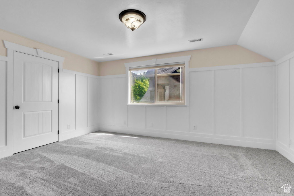 Unfurnished bedroom featuring a decorative wall, carpet flooring, and lofted ceiling
