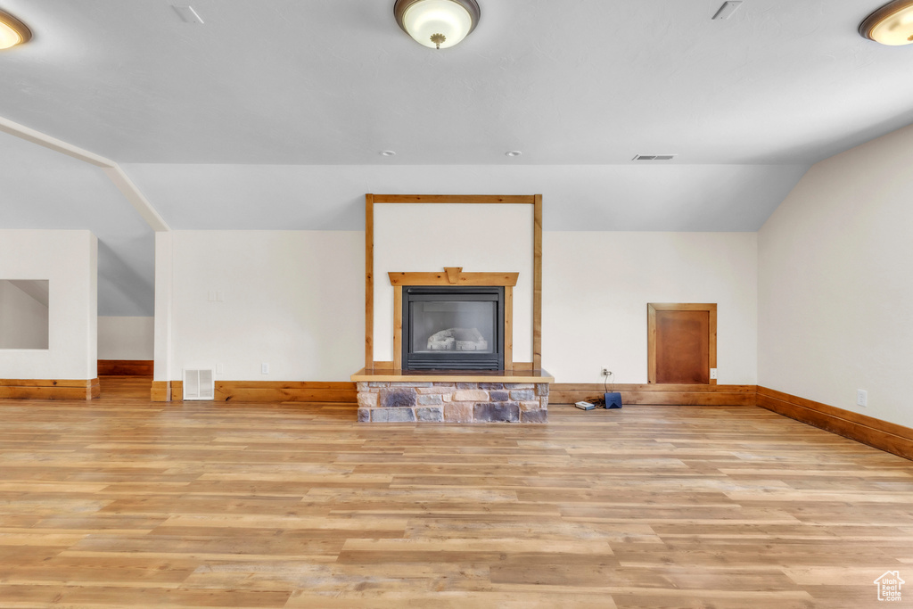 Unfurnished living room with vaulted ceiling, wood finished floors, and a fireplace