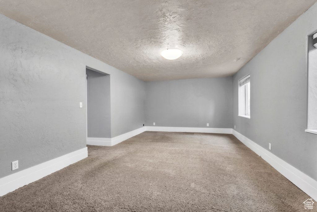 Carpeted empty room with a textured ceiling and baseboards