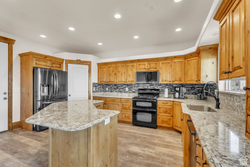 Kitchen featuring stainless steel appliances, a center island, tasteful backsplash, light stone countertops, and light wood-style floors