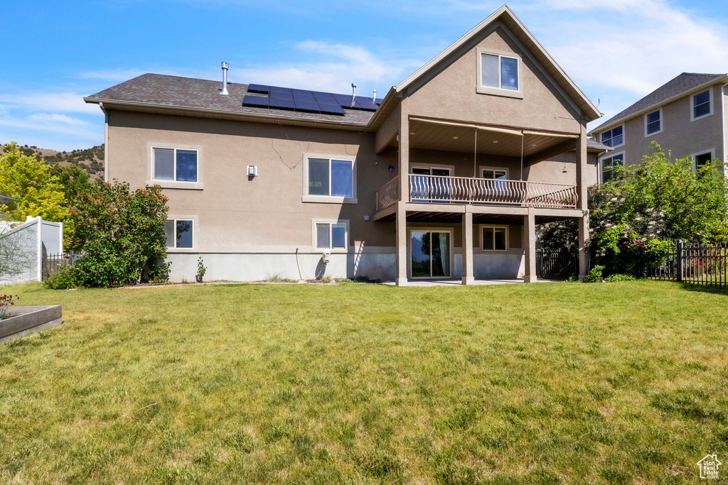 Back of property featuring roof mounted solar panels, stucco siding, a shingled roof, and a balcony