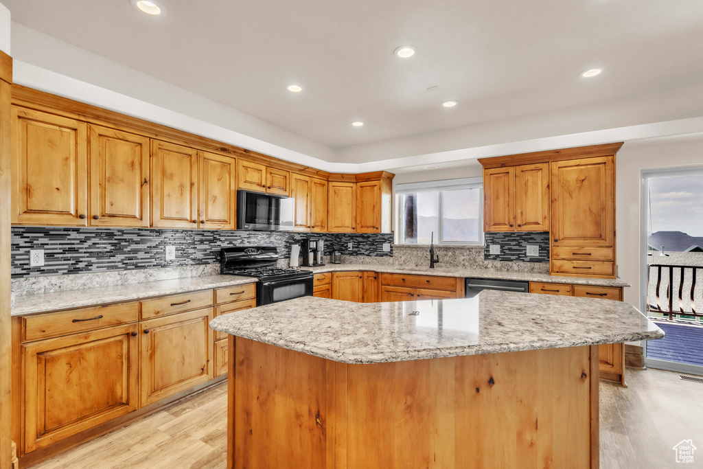 Kitchen featuring black appliances, light wood-type flooring, a center island, backsplash, and recessed lighting