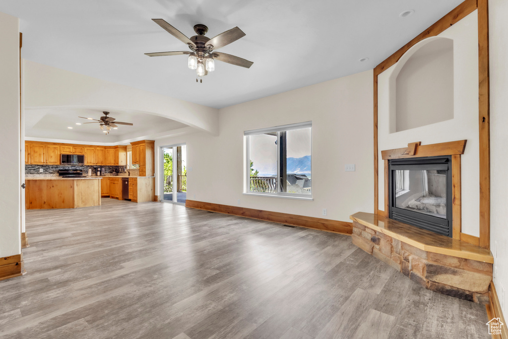 Unfurnished living room with light wood-type flooring, ceiling fan, a glass covered fireplace, and arched walkways