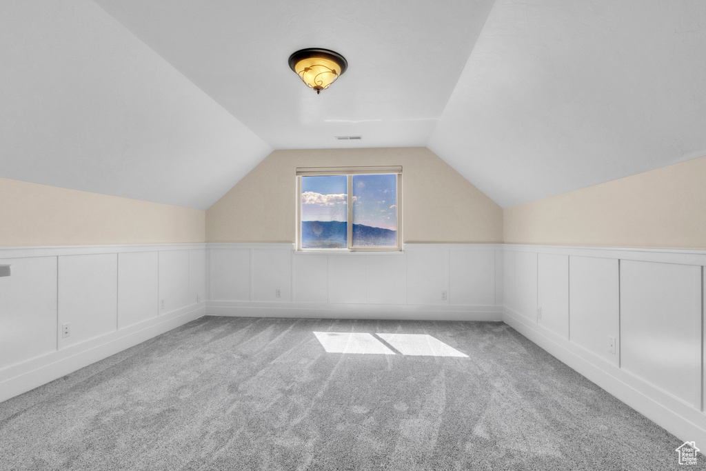 Additional living space with vaulted ceiling, carpet, a decorative wall, and wainscoting