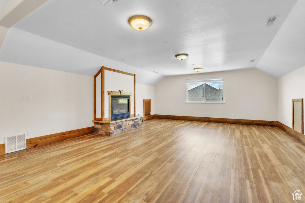 Bonus room featuring vaulted ceiling, light wood finished floors, and a stone fireplace