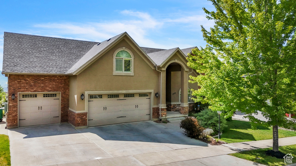 View of front of home with concrete driveway, stucco siding, stone siding, a front yard, and a shingled roof