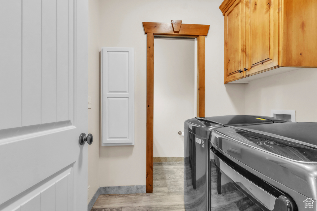 Washroom with washing machine and dryer, cabinet space, and wood finished floors