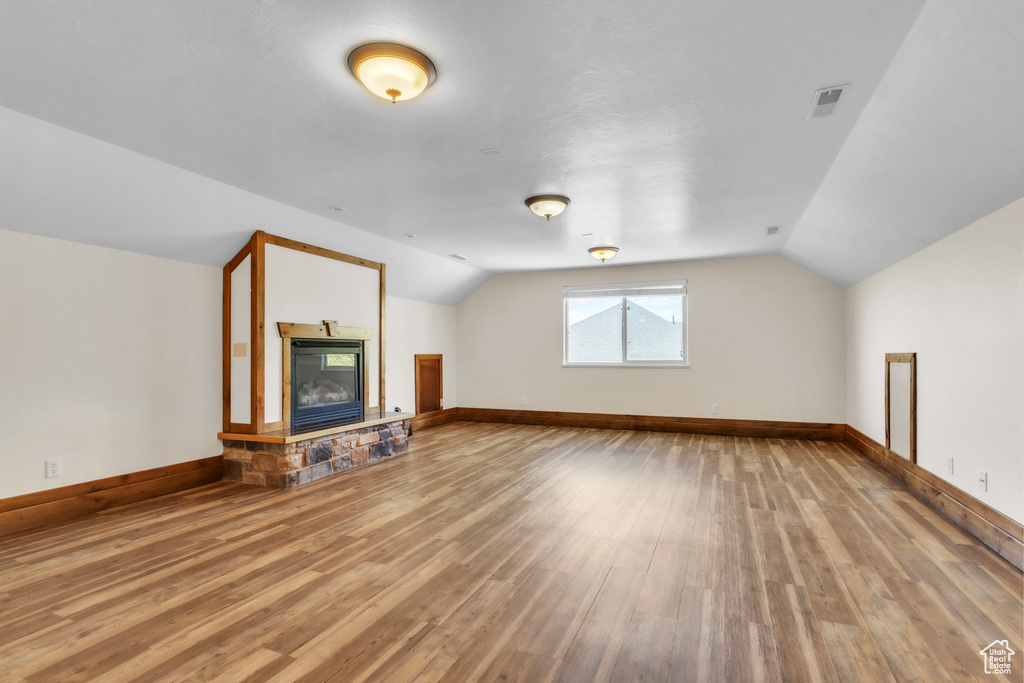 Unfurnished living room featuring lofted ceiling, wood finished floors, and a stone fireplace