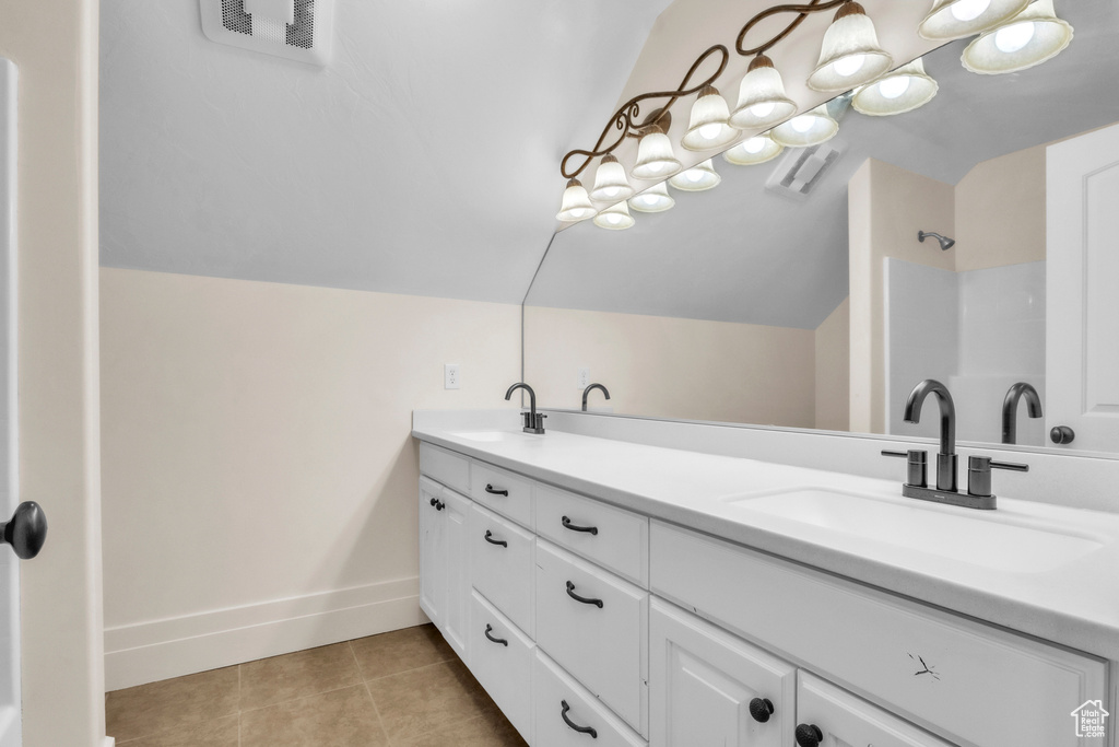 Bathroom featuring vaulted ceiling, double vanity, tile patterned floors, and a shower
