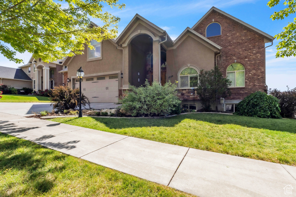 View of front of property with driveway, a front lawn, stucco siding, and brick siding
