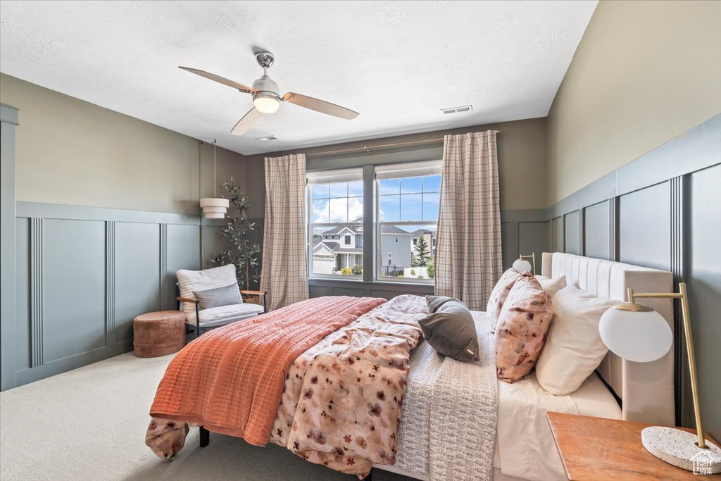 Bedroom featuring a decorative wall, a wainscoted wall, a ceiling fan, and carpet flooring