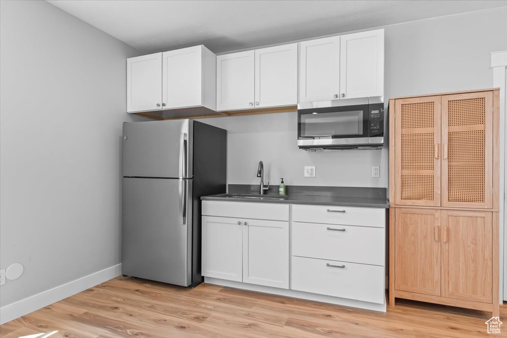 Kitchen with stainless steel appliances, dark countertops, light wood-type flooring, and white cabinetry