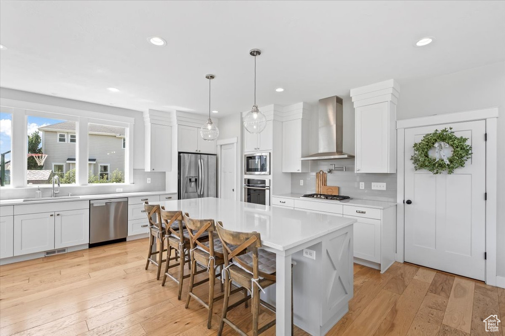 Kitchen with wall chimney exhaust hood, appliances with stainless steel finishes, light countertops, decorative backsplash, and recessed lighting