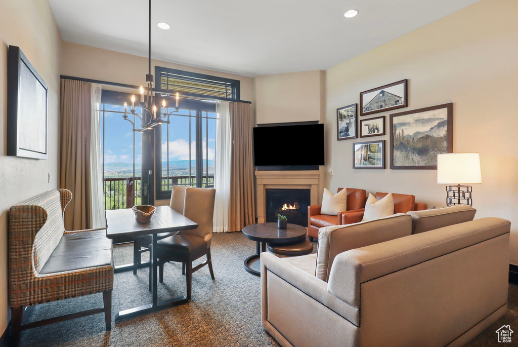 Living area with a chandelier, a warm lit fireplace, dark colored carpet, and recessed lighting