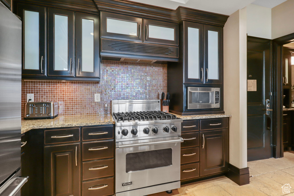 Kitchen with stainless steel appliances, tasteful backsplash, light stone counters, and glass insert cabinets