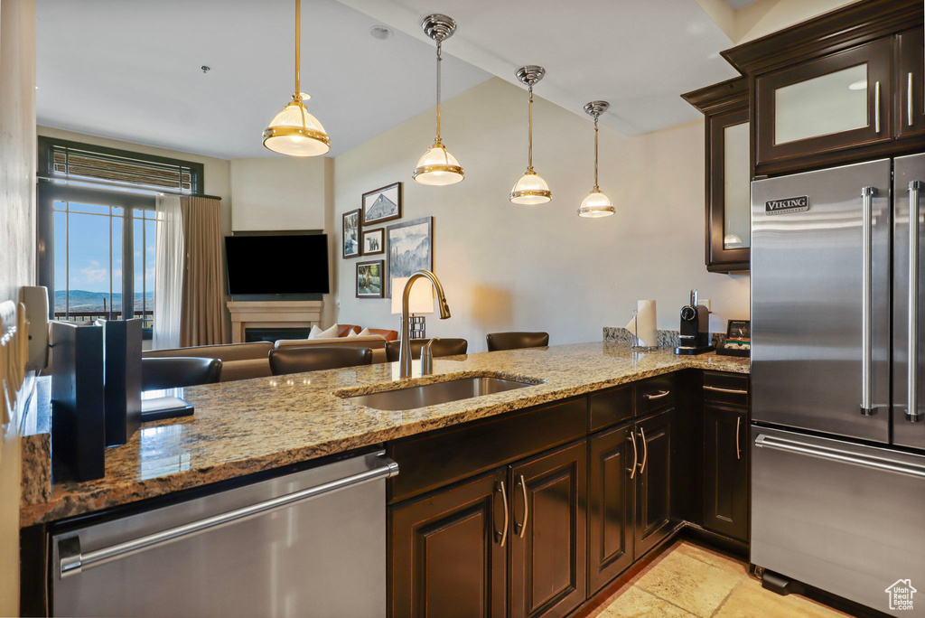 Kitchen with stainless steel appliances, light stone counters, glass insert cabinets, and dark brown cabinetry