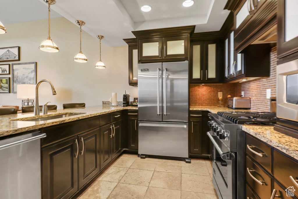Kitchen featuring high quality appliances, backsplash, glass insert cabinets, pendant lighting, and light stone countertops