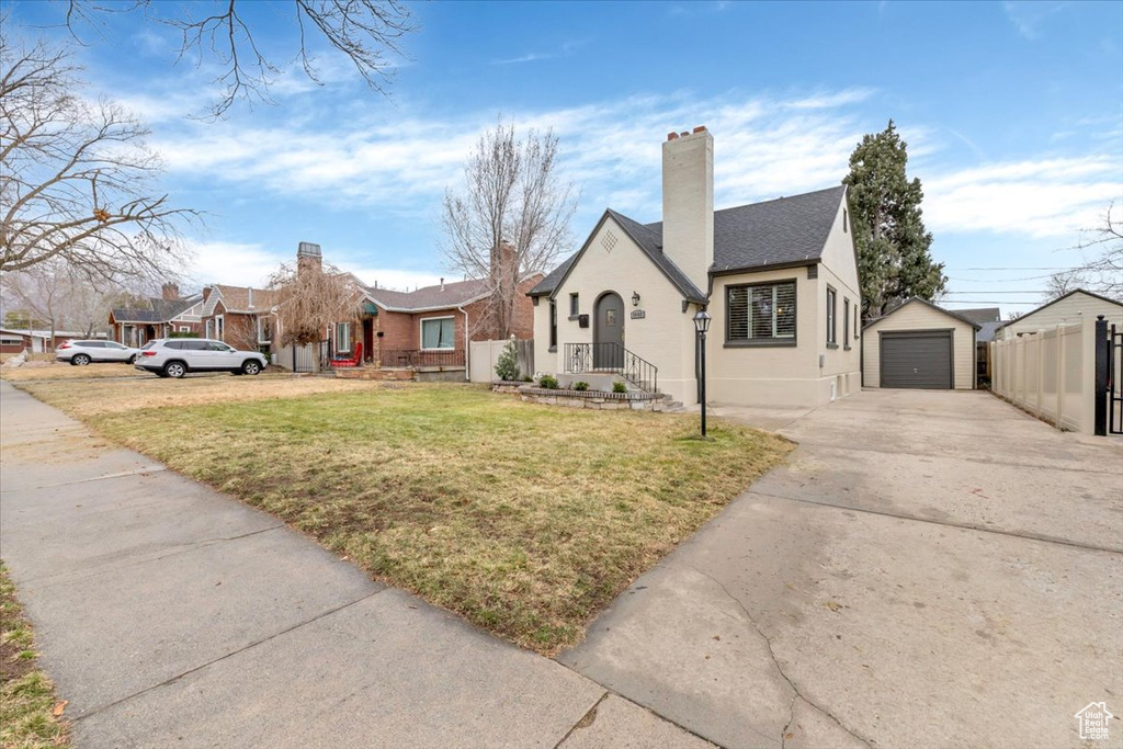 View of front facade with concrete driveway, a detached garage, an outbuilding, and a chimney
