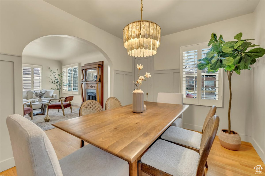 Dining space with arched walkways, light wood finished floors, healthy amount of natural light, a chandelier, and a decorative wall