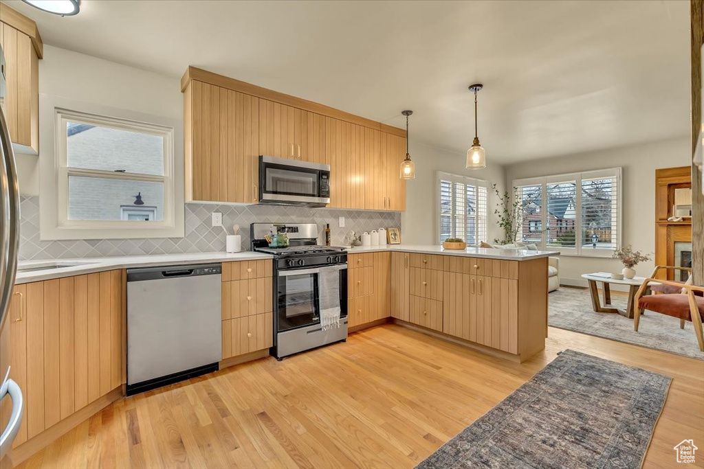 Kitchen with appliances with stainless steel finishes, light brown cabinets, light wood-style flooring, and decorative backsplash