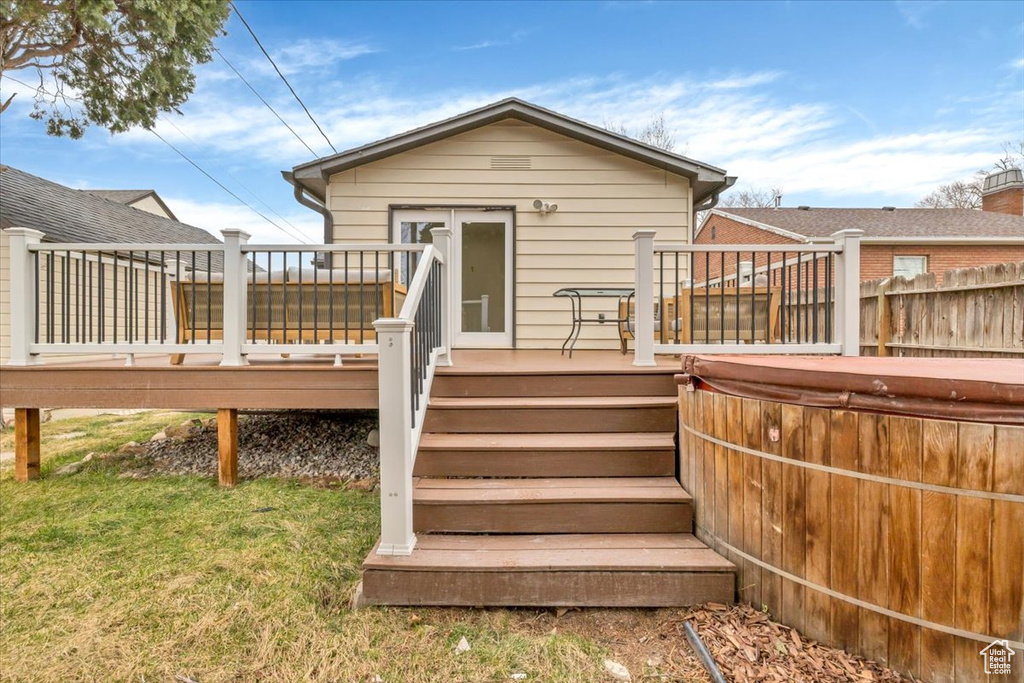 Back of property with a hot tub, a deck, a yard, and stairs