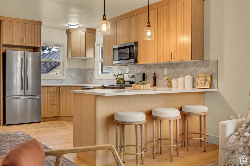Kitchen featuring stainless steel appliances, a peninsula, light wood finished floors, backsplash, and light countertops